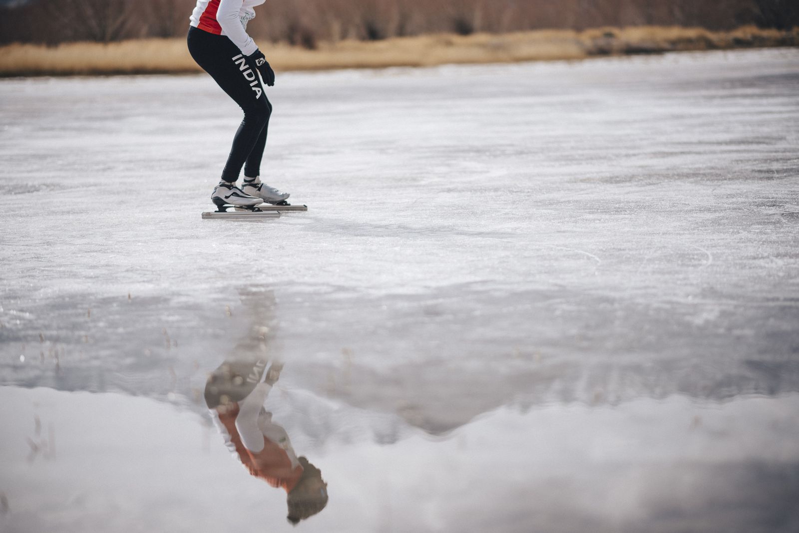 Vishwaraj's long-track blades on frozen lake ice, his reflection in the surface
